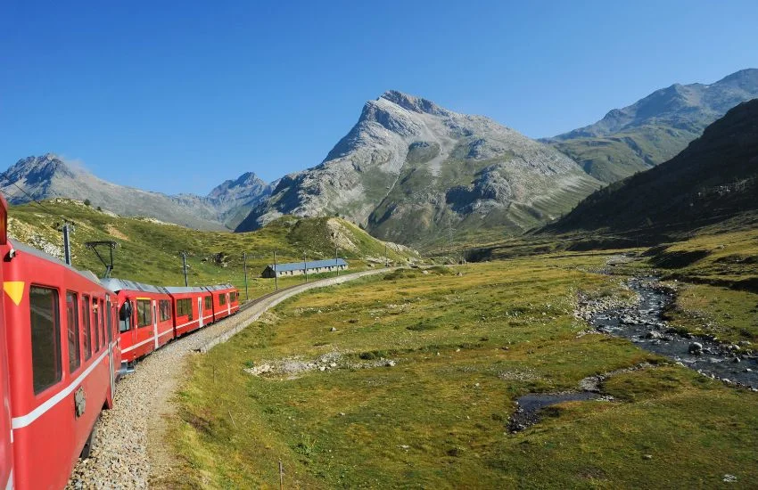 Tren rojo de Artouste recorriendo un paisaje de alta montaña en los Pirineos franceses, junto a un arroyo y rodeado de cumbres