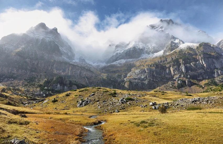 Paisaje del Valle de Tena con montañas nevadas, nubes bajas y pradera, ideal para disfrutar del columpio panorámico de Hoz de Jaca en los Pirineos aragoneses.