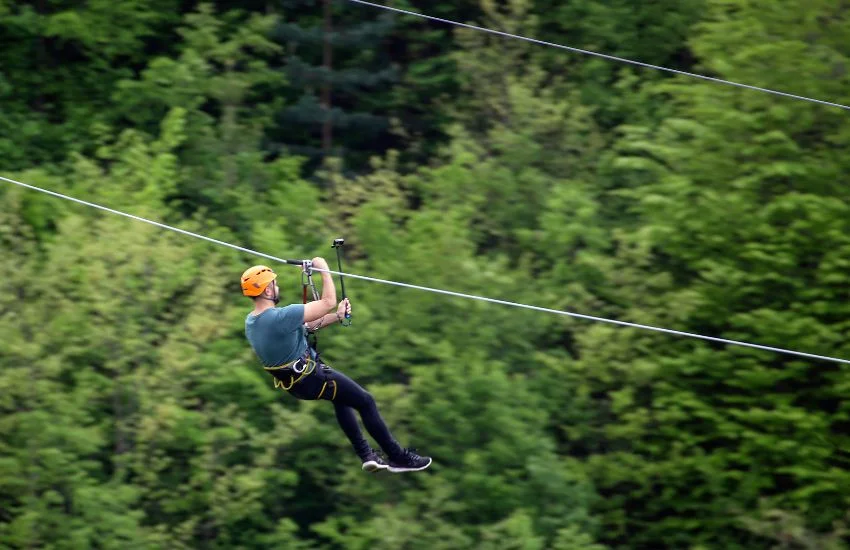 Deportes de aventura para liberar estrés: persona deslizándose en tirolina con montañas del Valle de Tena al fondo